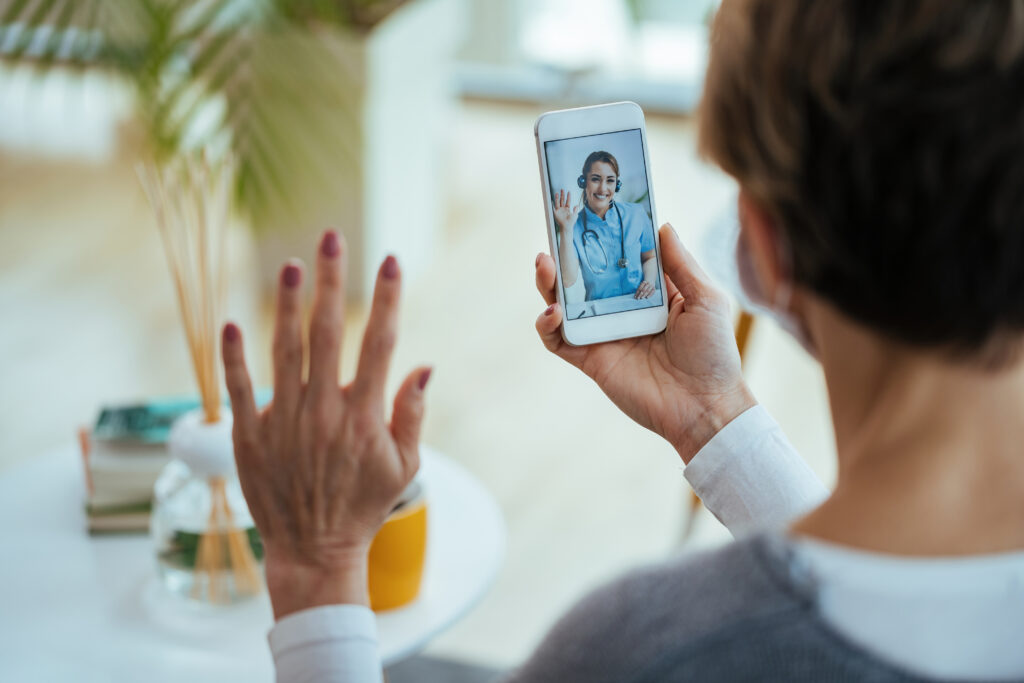 Home happy doctor waving while having video call with patient over mo