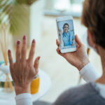 happy doctor waving while having video call with patient over mo